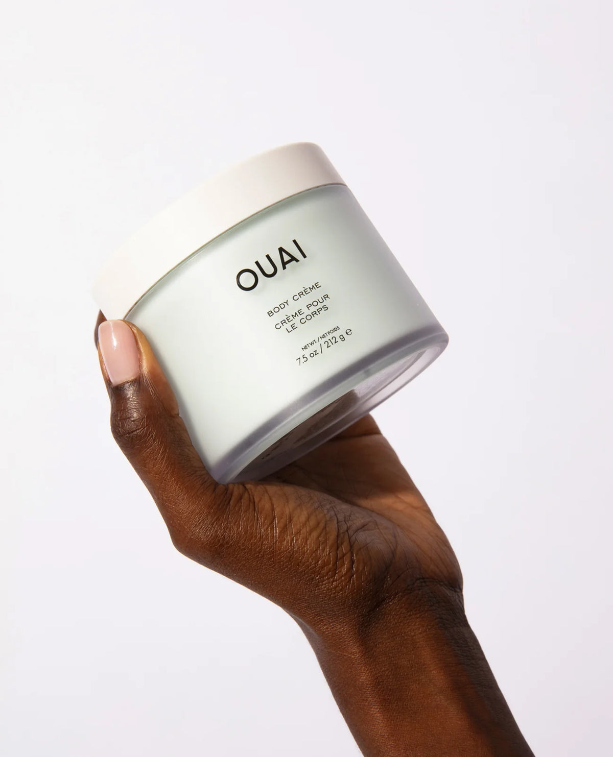 Hand holding a jar of OUAI body cream against a white background